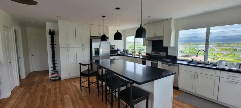 Bright kitchen with white cabinetry, black counters and a seating island facing large windows