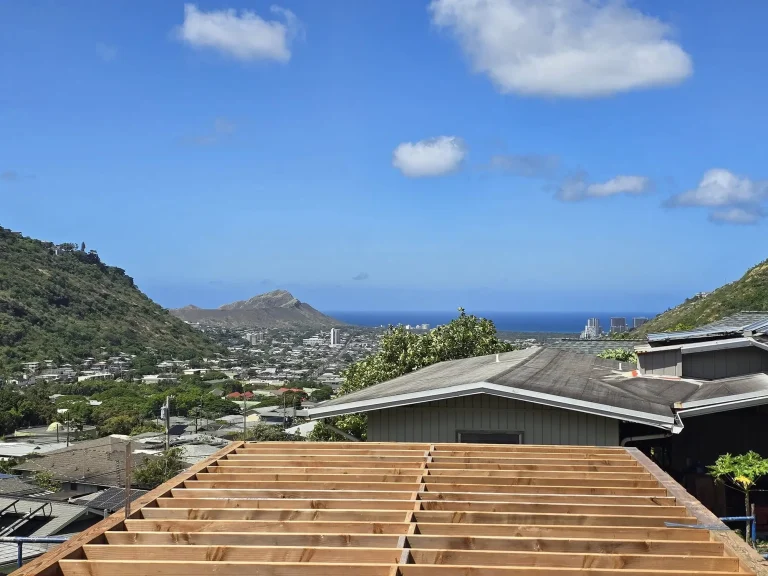 Roof framing in progress with a hillside neighborhood, Diamond Head and the ocean in the distance